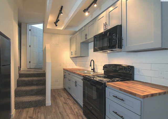 kitchen with gray cabinetry, butcher block countertops, dark wood-type flooring, black appliances, and tasteful backsplash