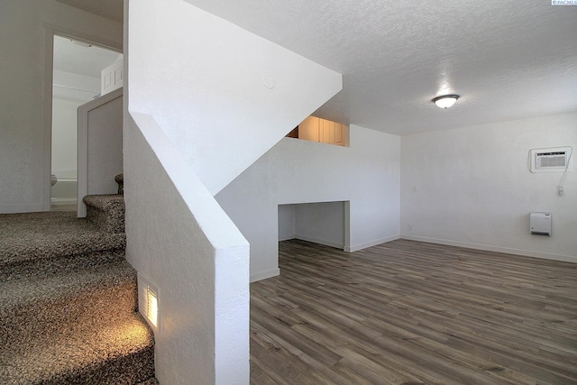 stairs featuring a textured ceiling, an AC wall unit, wood finished floors, and baseboards