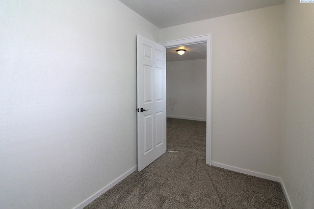 hallway with dark carpet and baseboards