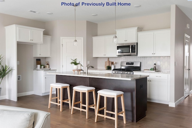 kitchen featuring appliances with stainless steel finishes, white cabinetry, a kitchen island with sink, and decorative light fixtures