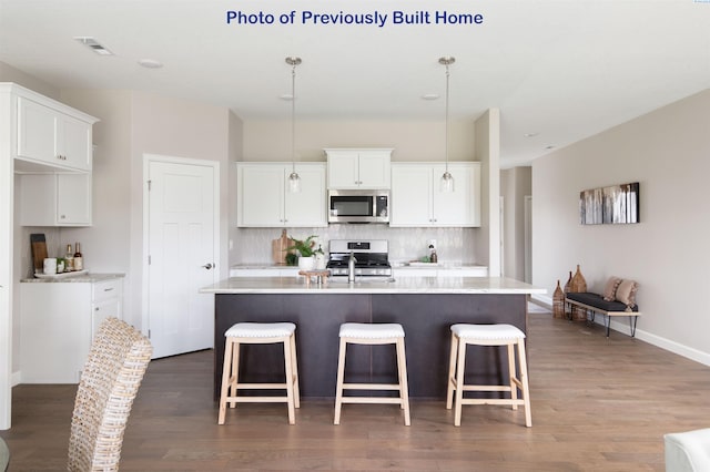 kitchen featuring light countertops, appliances with stainless steel finishes, an island with sink, and white cabinets