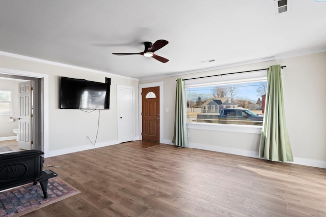 unfurnished living room with wood-type flooring, ornamental molding, a wood stove, and ceiling fan