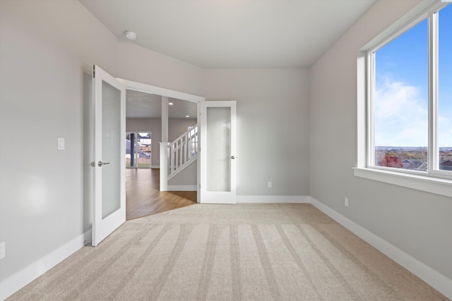 spare room with baseboards, light colored carpet, and french doors