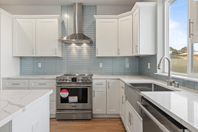 kitchen with wall chimney range hood, appliances with stainless steel finishes, white cabinets, and light wood finished floors