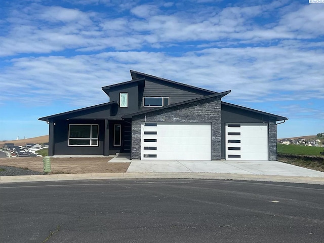 contemporary home with stone siding, an attached garage, and concrete driveway