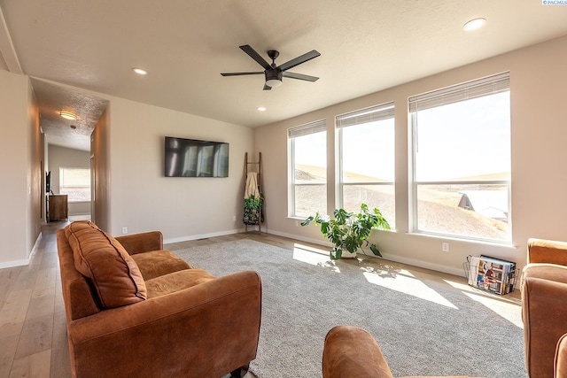 living room featuring light hardwood / wood-style flooring, ceiling fan, and a textured ceiling