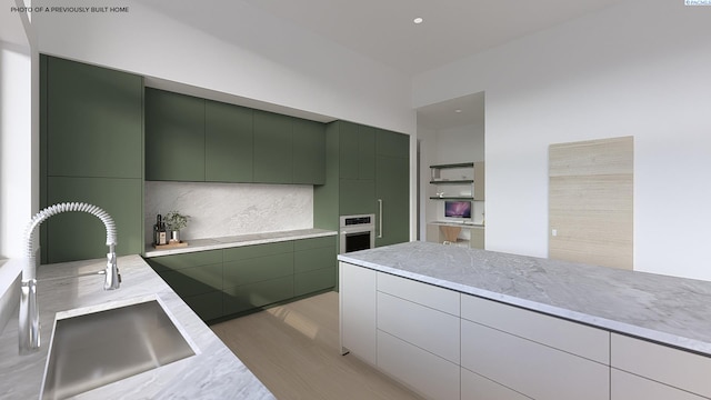 kitchen featuring modern cabinets, a sink, decorative backsplash, green cabinetry, and light wood-style floors