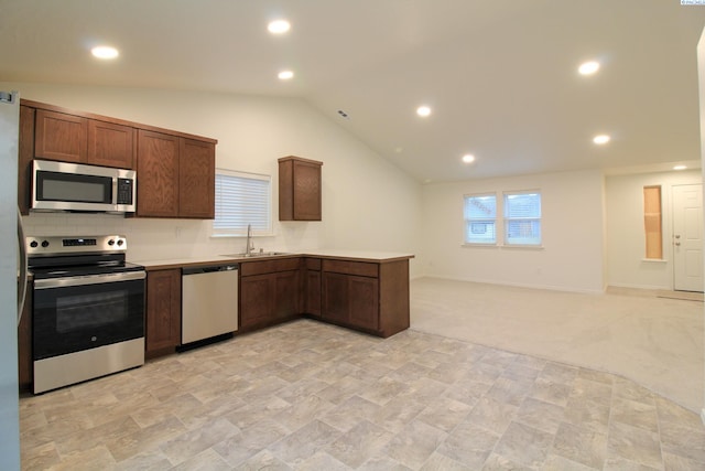 kitchen with appliances with stainless steel finishes, lofted ceiling, sink, light colored carpet, and kitchen peninsula