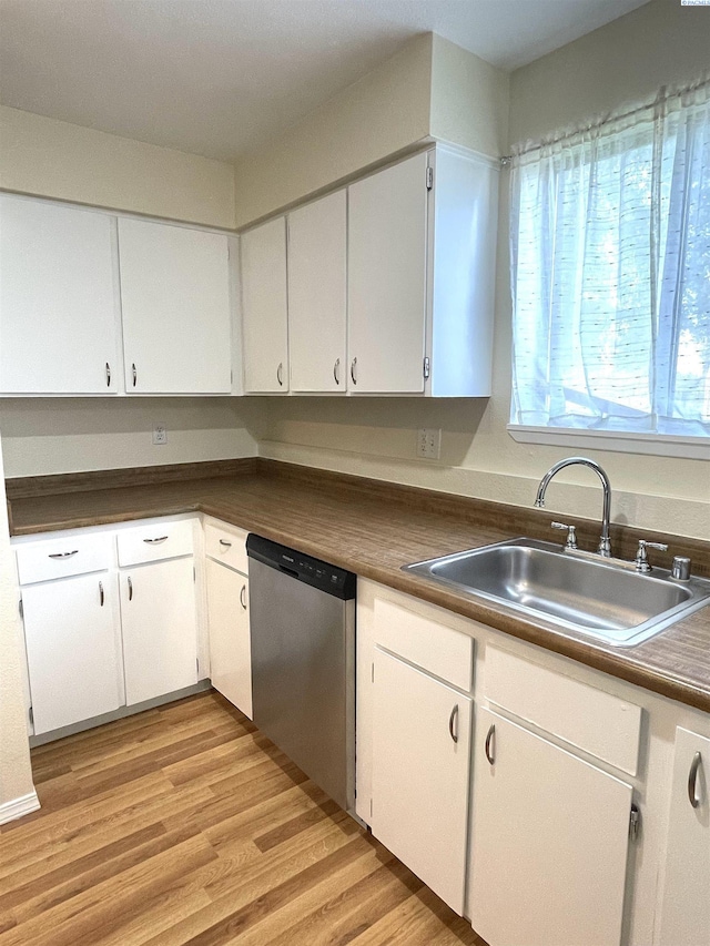 kitchen with dark countertops, white cabinetry, stainless steel dishwasher, and a sink
