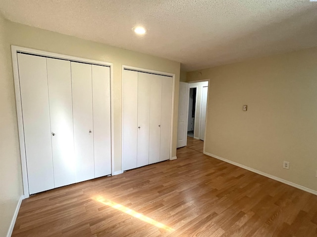 unfurnished bedroom with light wood finished floors, two closets, baseboards, and a textured ceiling