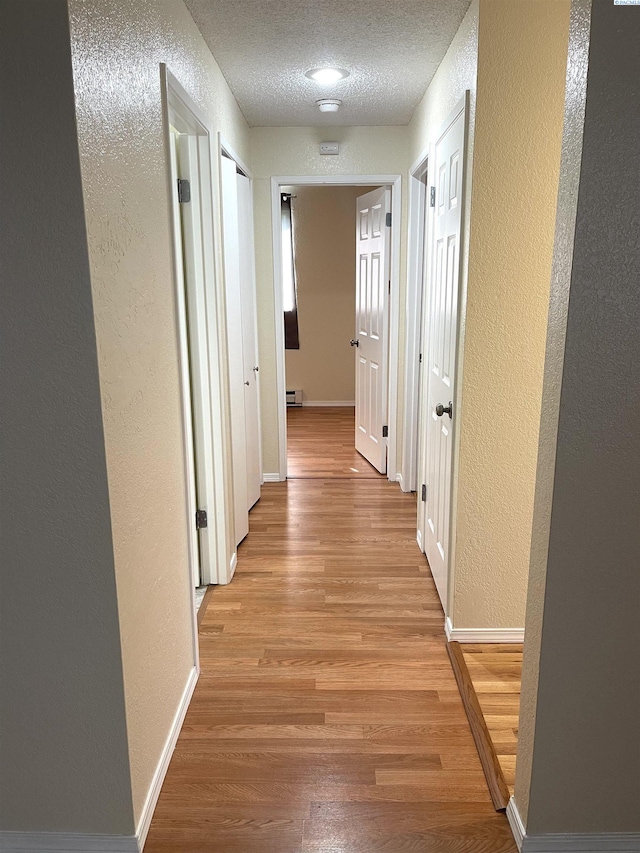 hallway with a textured ceiling, light wood-style flooring, baseboards, and a textured wall