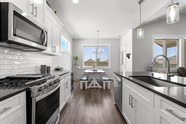 kitchen with a sink, dark wood finished floors, a chandelier, dark countertops, and appliances with stainless steel finishes