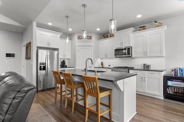 kitchen featuring a sink, a kitchen breakfast bar, dark countertops, appliances with stainless steel finishes, and dark wood-style floors
