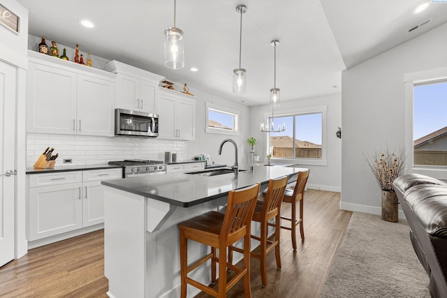 kitchen featuring stainless steel microwave, a sink, visible vents, range, and dark countertops