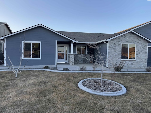 ranch-style home featuring stone siding, a patio, a shingled roof, and a front lawn