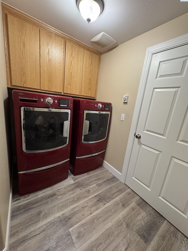 laundry room featuring baseboards, light wood-style flooring, separate washer and dryer, cabinet space, and a textured ceiling