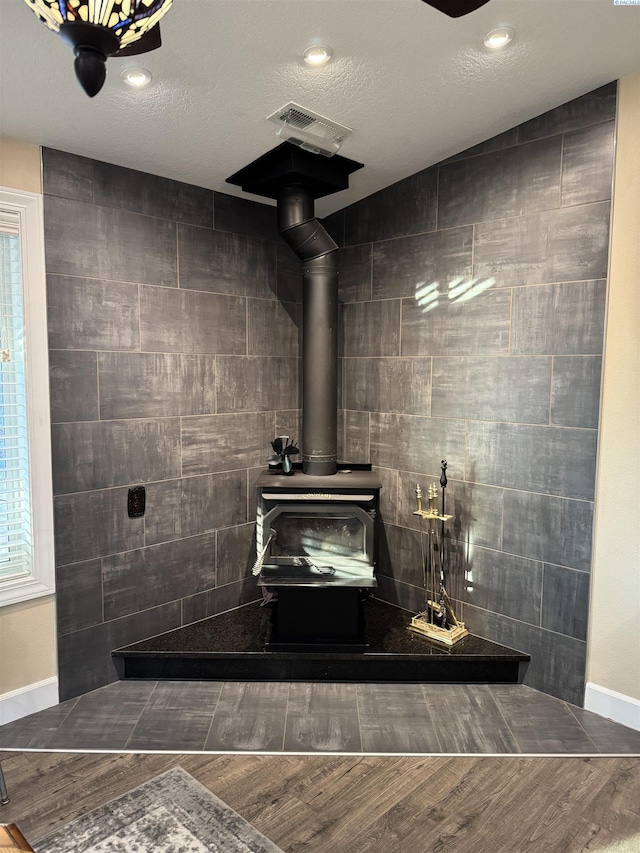 interior details with visible vents, a textured ceiling, a wood stove, and wood finished floors