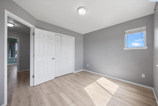 unfurnished bedroom with light wood finished floors, baseboards, and a closet