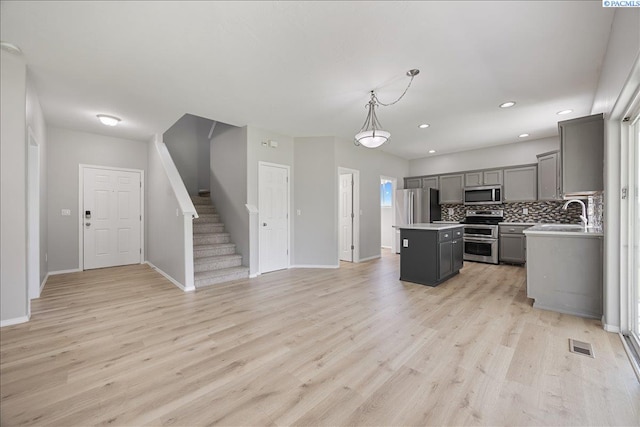 kitchen featuring appliances with stainless steel finishes, gray cabinetry, a kitchen island, light countertops, and open floor plan