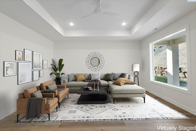 living room with hardwood / wood-style flooring, a raised ceiling, and ceiling fan