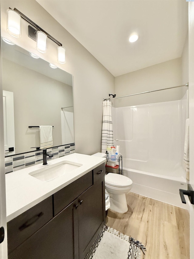 full bath with toilet, wood finished floors, shower / bathtub combination with curtain, vanity, and backsplash