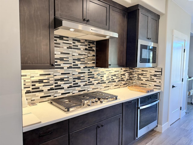 kitchen with appliances with stainless steel finishes, decorative backsplash, dark brown cabinetry, and under cabinet range hood