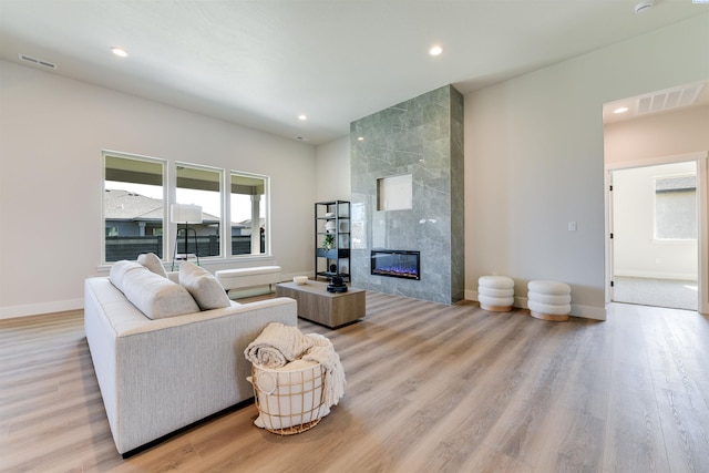living area with visible vents, a high end fireplace, baseboards, recessed lighting, and light wood-style floors
