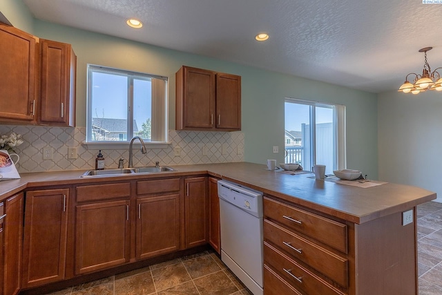 kitchen featuring white dishwasher, an inviting chandelier, a sink, a peninsula, and backsplash