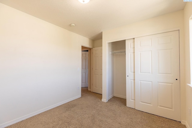 unfurnished bedroom featuring baseboards, light colored carpet, and a closet