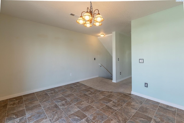 empty room with stone finish flooring, a textured ceiling, visible vents, baseboards, and a notable chandelier