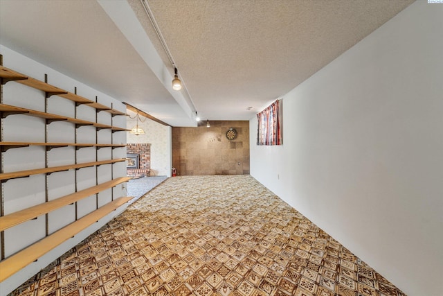 finished basement featuring rail lighting, a brick fireplace, and a textured ceiling