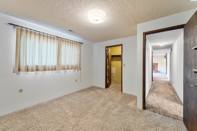 unfurnished bedroom with visible vents, light colored carpet, a spacious closet, a textured ceiling, and a closet