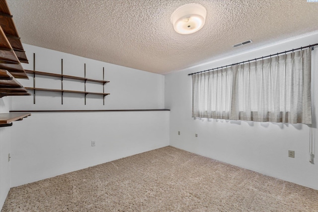 unfurnished room with carpet, visible vents, and a textured ceiling