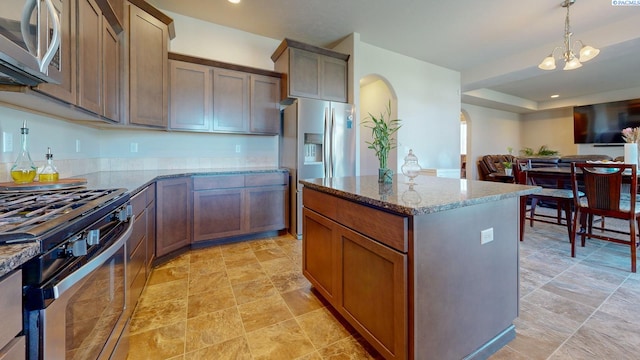 5802 Sidon Ln, Pasco, WA 99301 - kitchen with arched walkways, stainless steel appliances, light stone counters, a center island, and decorative light fixtures