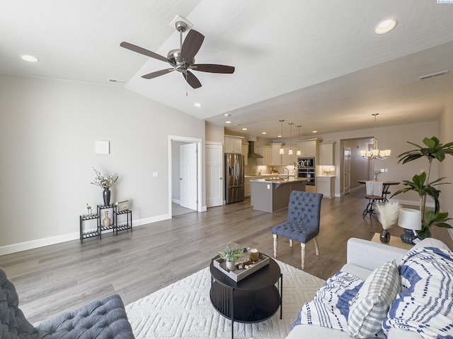 living area with visible vents, baseboards, lofted ceiling, light wood-style flooring, and ceiling fan with notable chandelier