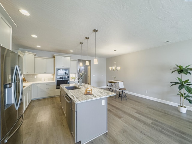 kitchen with appliances with stainless steel finishes, light wood-type flooring, a sink, and tasteful backsplash