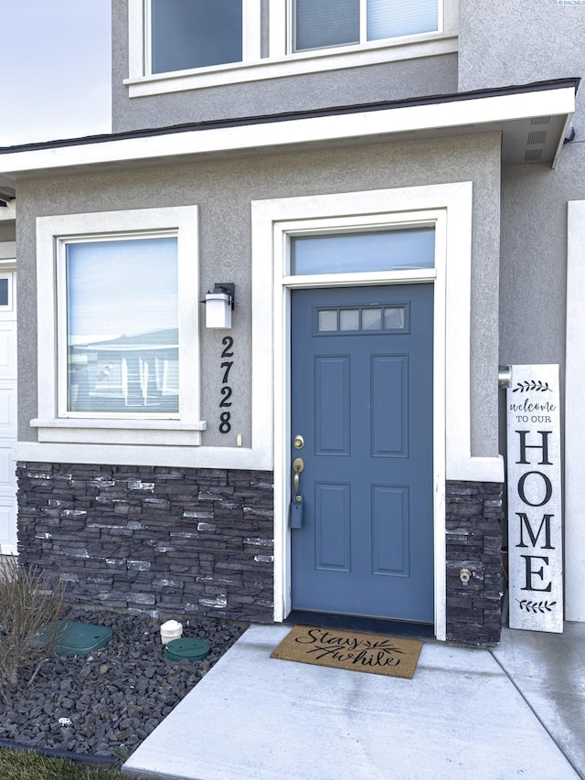 doorway to property featuring stone siding and stucco siding