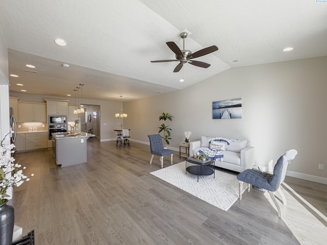 living area with recessed lighting, ceiling fan with notable chandelier, baseboards, vaulted ceiling, and light wood-style floors