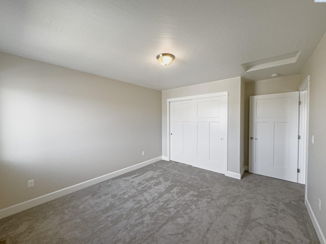 unfurnished bedroom featuring dark colored carpet, a closet, and baseboards