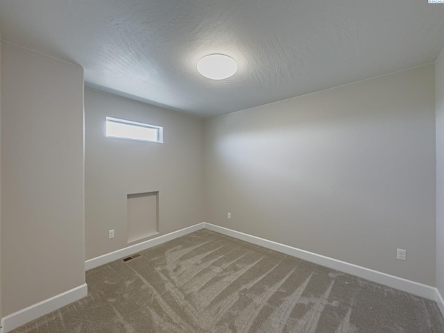 empty room with carpet, a textured ceiling, visible vents, and baseboards