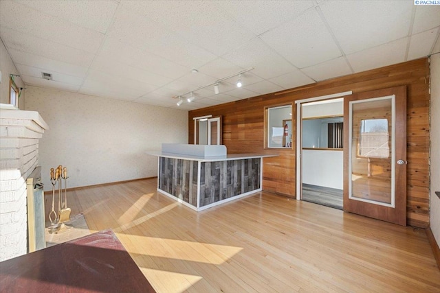 bar featuring a paneled ceiling, light wood-style flooring, wooden walls, and a fireplace