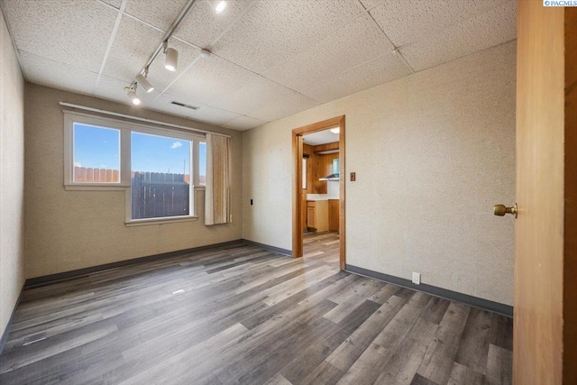 empty room featuring a paneled ceiling, visible vents, baseboards, and wood finished floors