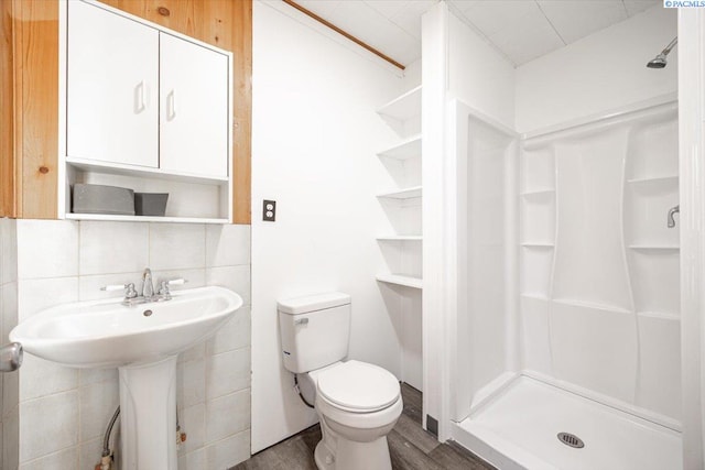 bathroom featuring toilet, decorative backsplash, a sink, a shower stall, and wood finished floors