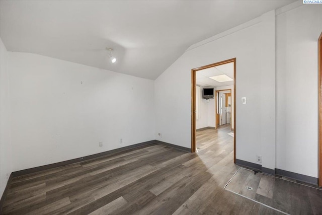 spare room featuring dark wood-type flooring, lofted ceiling, and baseboards