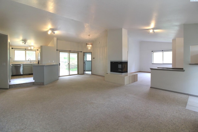 unfurnished living room with a sink, lofted ceiling, light carpet, and a healthy amount of sunlight