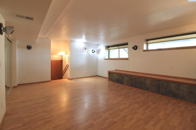 spare room featuring light wood-style floors, baseboards, visible vents, and a textured ceiling