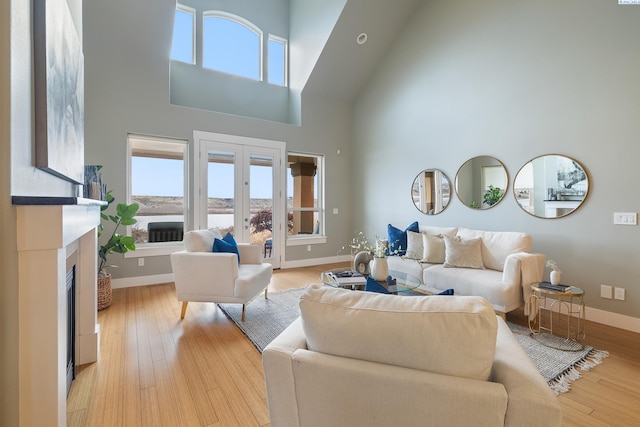 living room with french doors, a towering ceiling, and light hardwood / wood-style floors