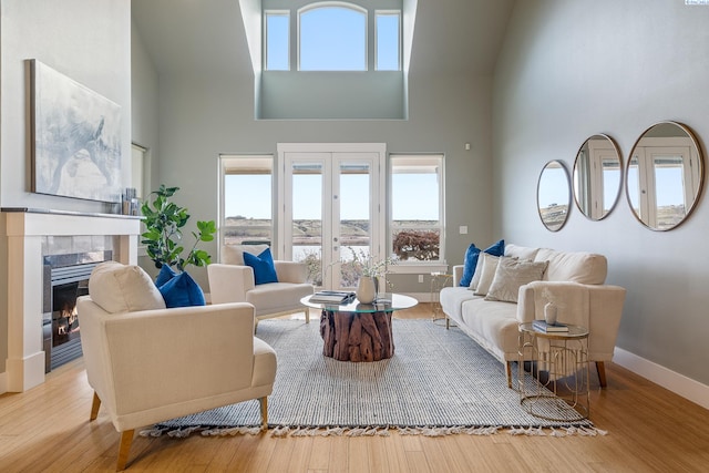 living room featuring french doors, a tiled fireplace, light hardwood / wood-style flooring, and a high ceiling