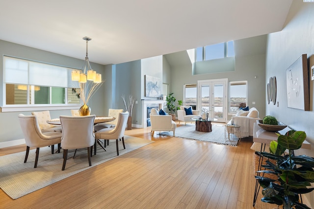 dining area with a tile fireplace, a towering ceiling, a notable chandelier, light hardwood / wood-style floors, and french doors