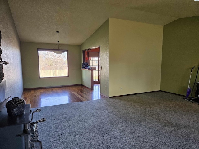 unfurnished dining area with lofted ceiling, carpet flooring, a textured ceiling, and baseboards